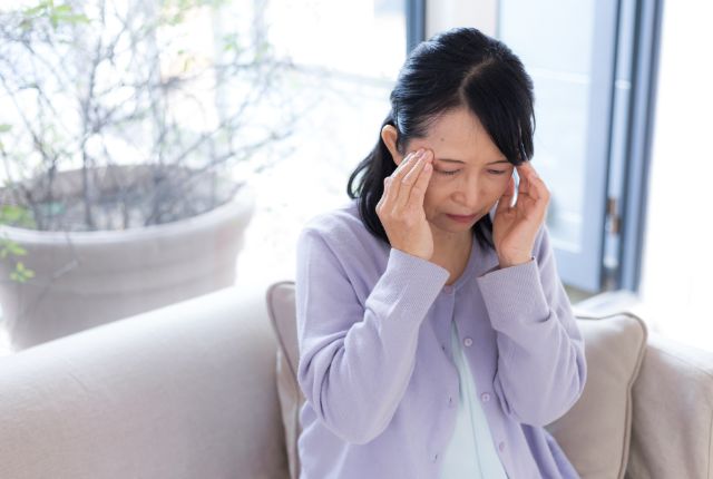 こめかみに手を当てて辛そうにしている女性