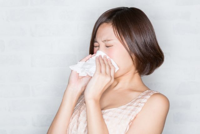 鼻をかみながら辛そうにしている女性